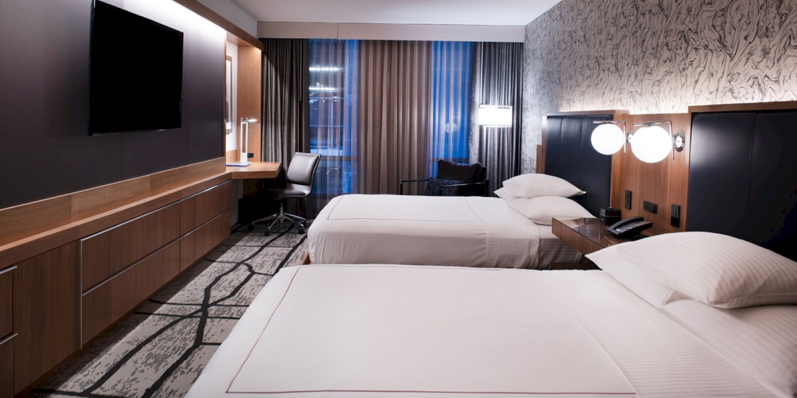 A modern hotel room with two neatly made beds, a flat-screen TV, a desk with a chair, and contemporary decor ending the sentence.