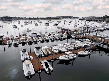 A marina filled with numerous boats docked in slips, with more boats anchored in the distance under a partly cloudy sky.