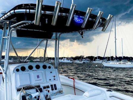 The image shows a boat's control area with white seats and instruments. The boat is on the water with other vessels and stormy skies in the background.