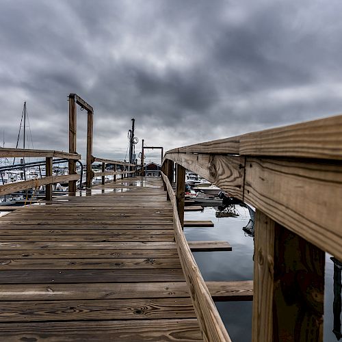 A wooden pier extends over a body of water under a cloudy sky, with boats docked on the left.