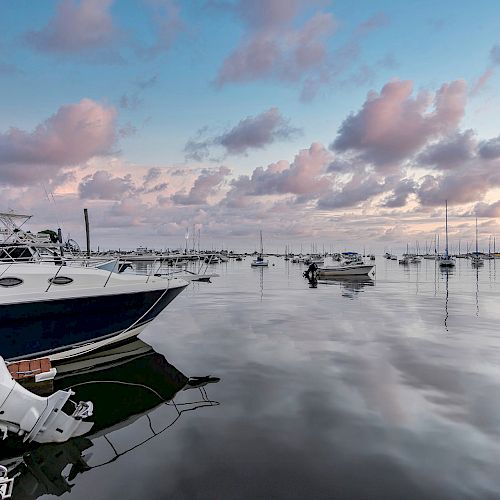 A serene marina at sunset with boats docked, calm water reflecting the sky, and an American flag on a nearby boat.