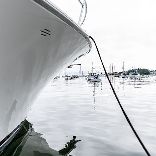 A close-up of a boat's bow tied to a mooring line, with other boats docked in a calm harbor in the background, ending the sentence.