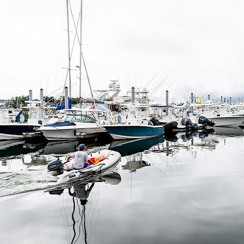 Several boats are docked at a marina while a small inflatable boat with two people on board moves through the calm water in the foreground.