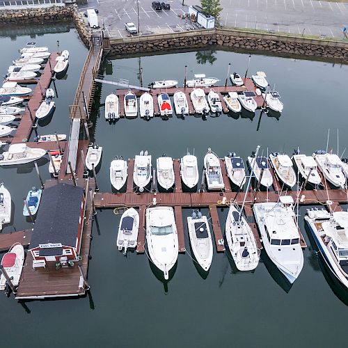 This image shows a marina with numerous boats docked at wooden piers, with a small building on one of the piers.