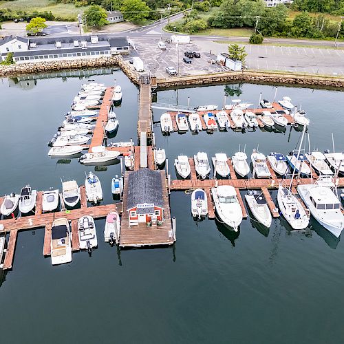 An aerial view of a marina with numerous boats docked, surrounded by calm water and nearby parking areas ending the sentence.