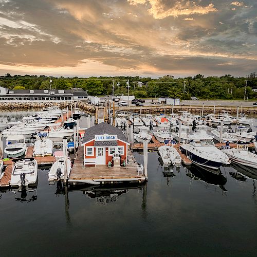 The image shows a marina with various anchored boats, a “Fuel Dock” building on the pier, and a scenic sunset in the background.