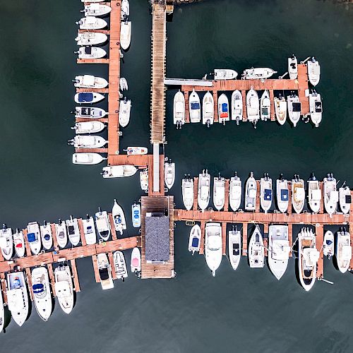 The image shows an aerial view of a marina with many boats docked along wooden piers over the water, arranged neatly in rows.