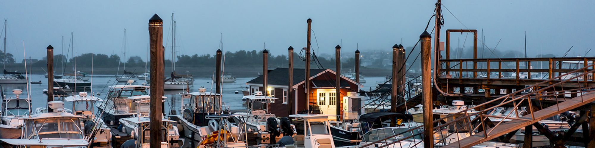 The image depicts a marina with numerous boats docked, a small house nearby, and a wooden pier extending into the water.