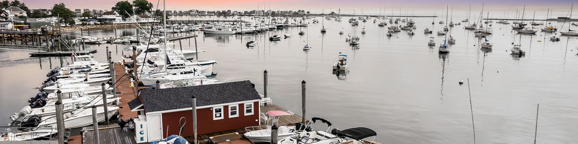 A marina at sunset, with numerous boats docked and anchored, calm waters reflecting the vibrant sky.